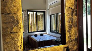 A bathroom with a stone wall, a large sink, a bathtub, and a window with vertical blinds.