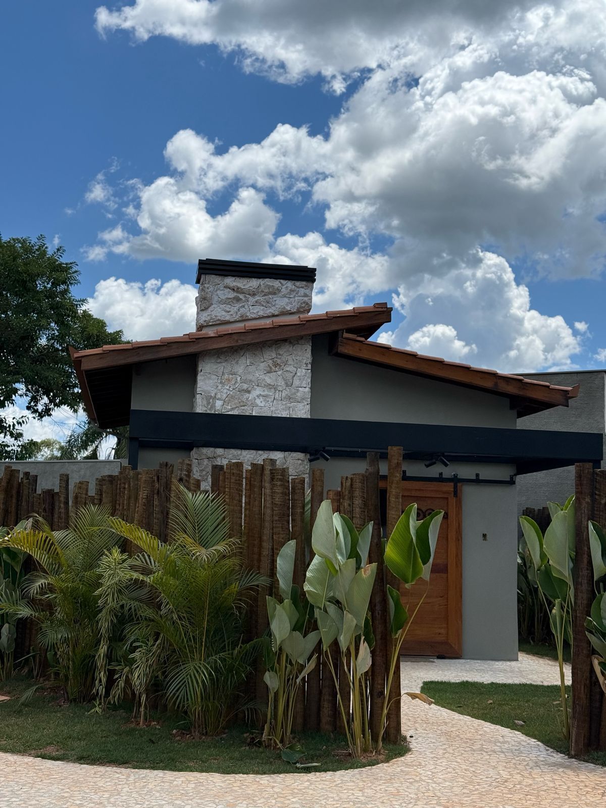 Une maison moderne avec une façade en pierre, une clôture en bois et des plantes tropicales.