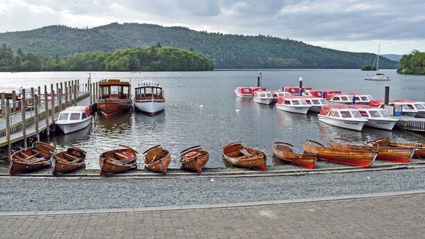 A marina with various boats docked, a wooden pier, and a forested hill in the background. - 2 bedroom accommodation in Bowness-on-Windermere (Bowness-on-Windermere)