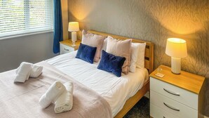 A neatly made bed with a patterned bedspread and two towels, two pillows, and a bedside table with a lamp. - 2 bedroom accommodation in Bowness-on-Windermere (Bowness-on-Windermere)