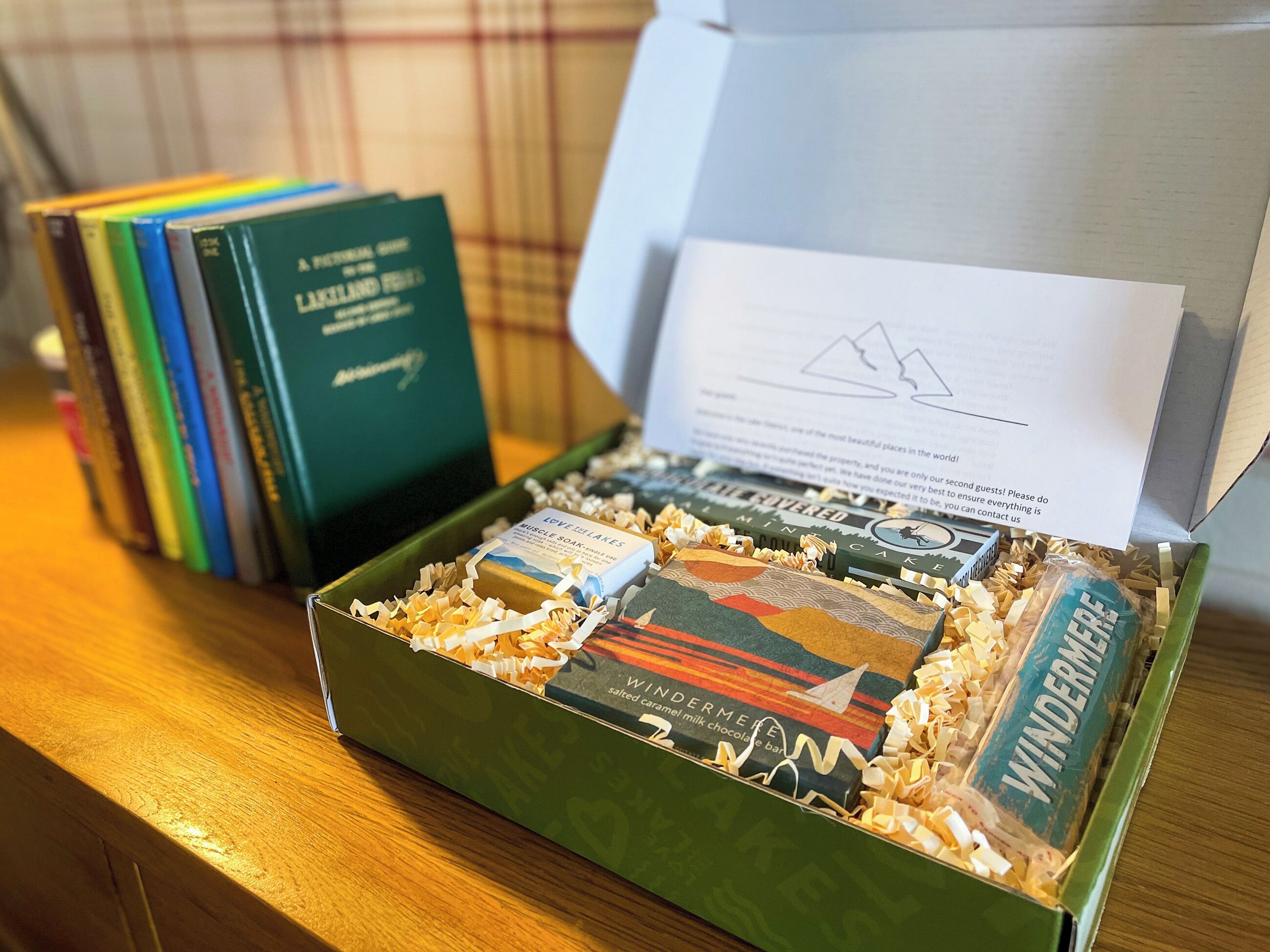A box of chocolates and books on a wooden table.
