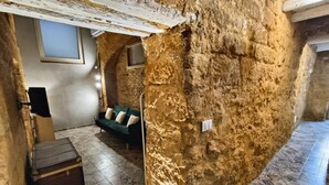A room with a rustic stone wall, a green sofa, patterned floor tiles, and a small wooden chest. - Historic Apartment (Agrigento)