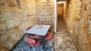 A stone-walled room with a white table and red chairs, a patterned floor, and a doorway leading to another room. - Historic Apartment (Agrigento)