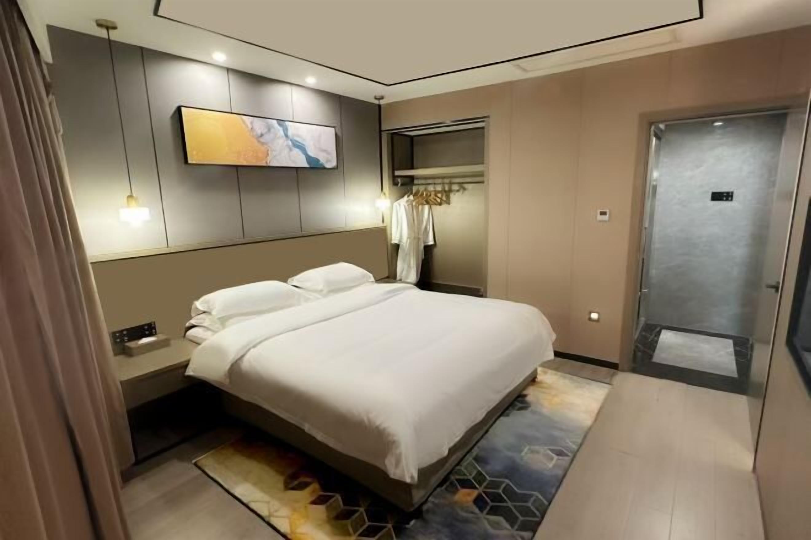 A modern hotel room with a large bed, a bedside table, a wall-mounted TV, and a wardrobe with hanging clothes.