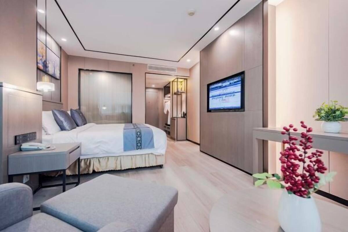 A modern hotel room with a bed, bedside table, TV, and a small seating area.
