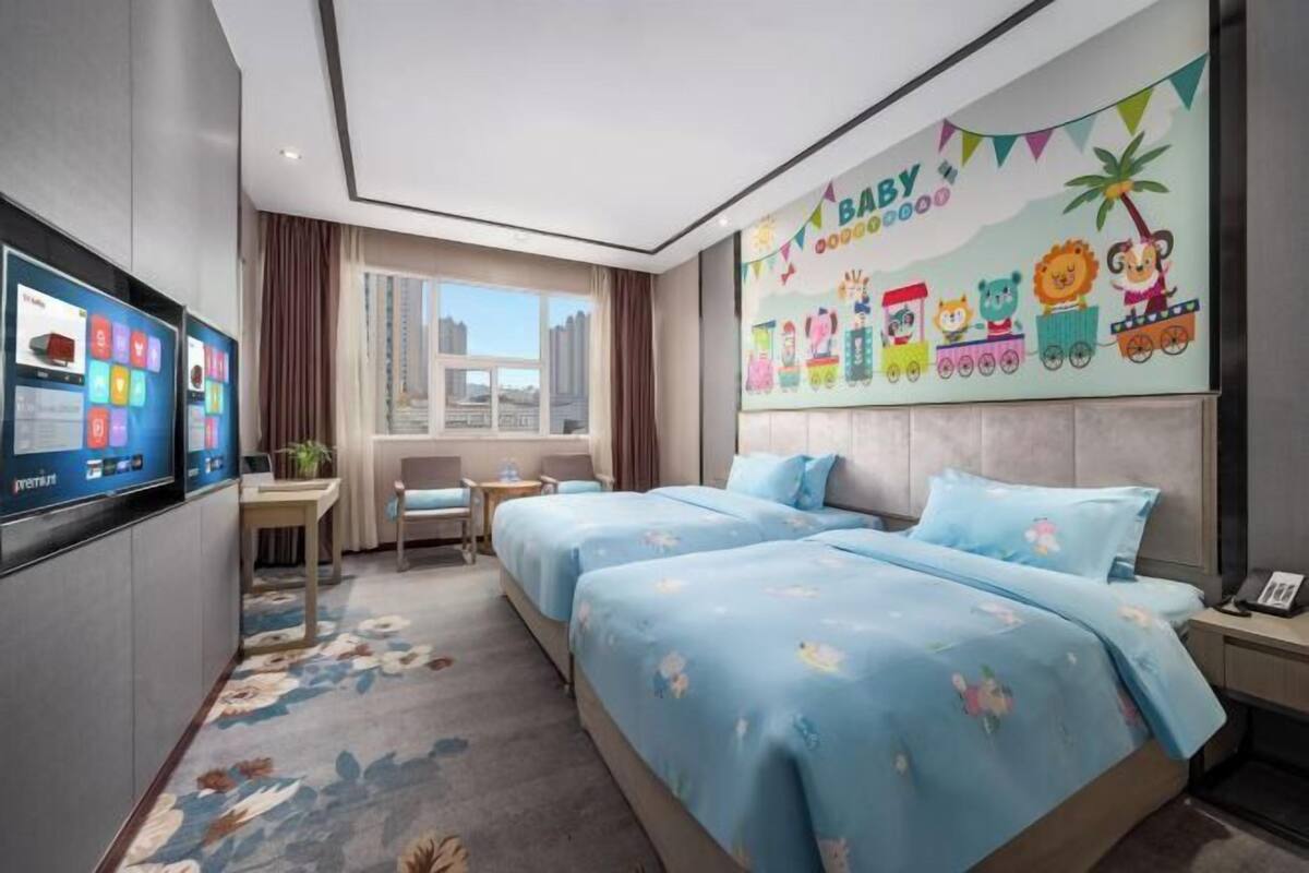 A hotel room with two beds, a TV, a desk, a chair, a window, and a wall mural.