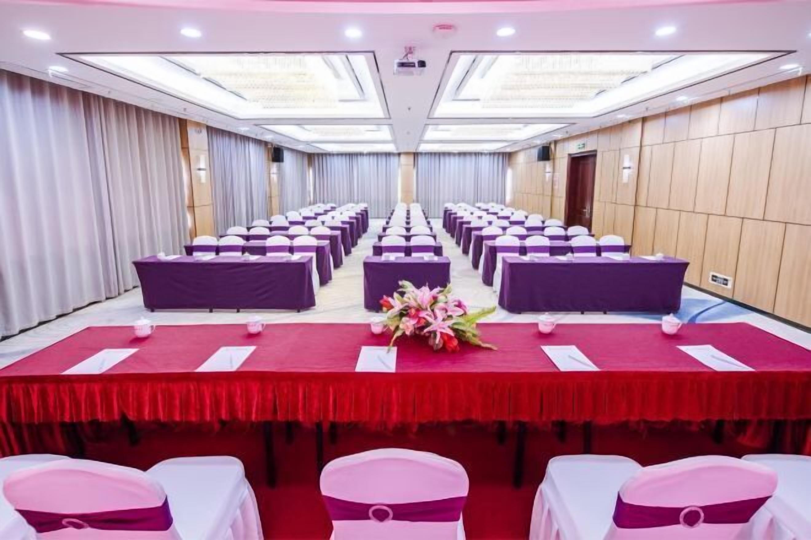 A conference room with rows of tables and chairs, a red tablecloth, and a floral centerpiece.