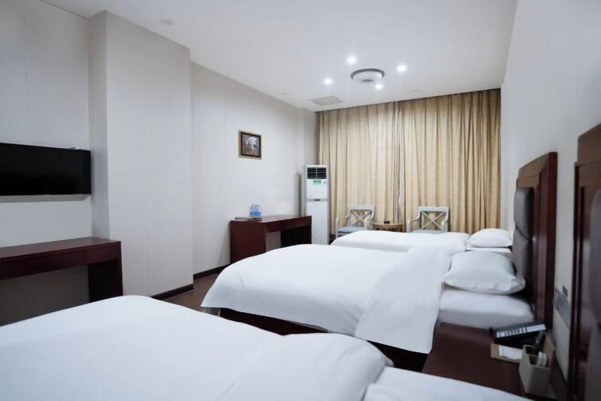 A hotel room with two beds, a desk, a chair, a TV, and a window with curtains.