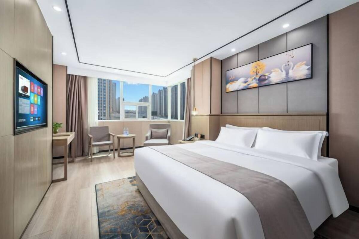 A hotel room with a large bed, a desk, a chair, a TV, and a painting on the wall.