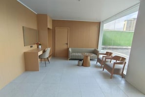 A modern living room with a sofa, a dining table, and chairs. There is a door and a window with a view of a building. - Qianmei Hotel (Ganzhou)