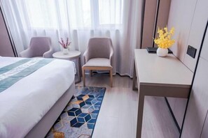 Une chambre d’hôtel comprenant un lit, deux fauteuils, une petite table ronde avec un vase et un bureau également agrémenté d’un vase.