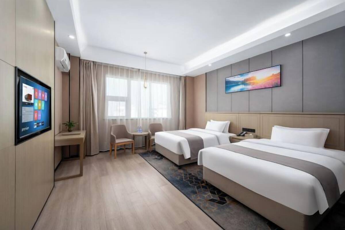 A hotel room with two beds, a desk, a chair, a TV, and a large window with curtains.