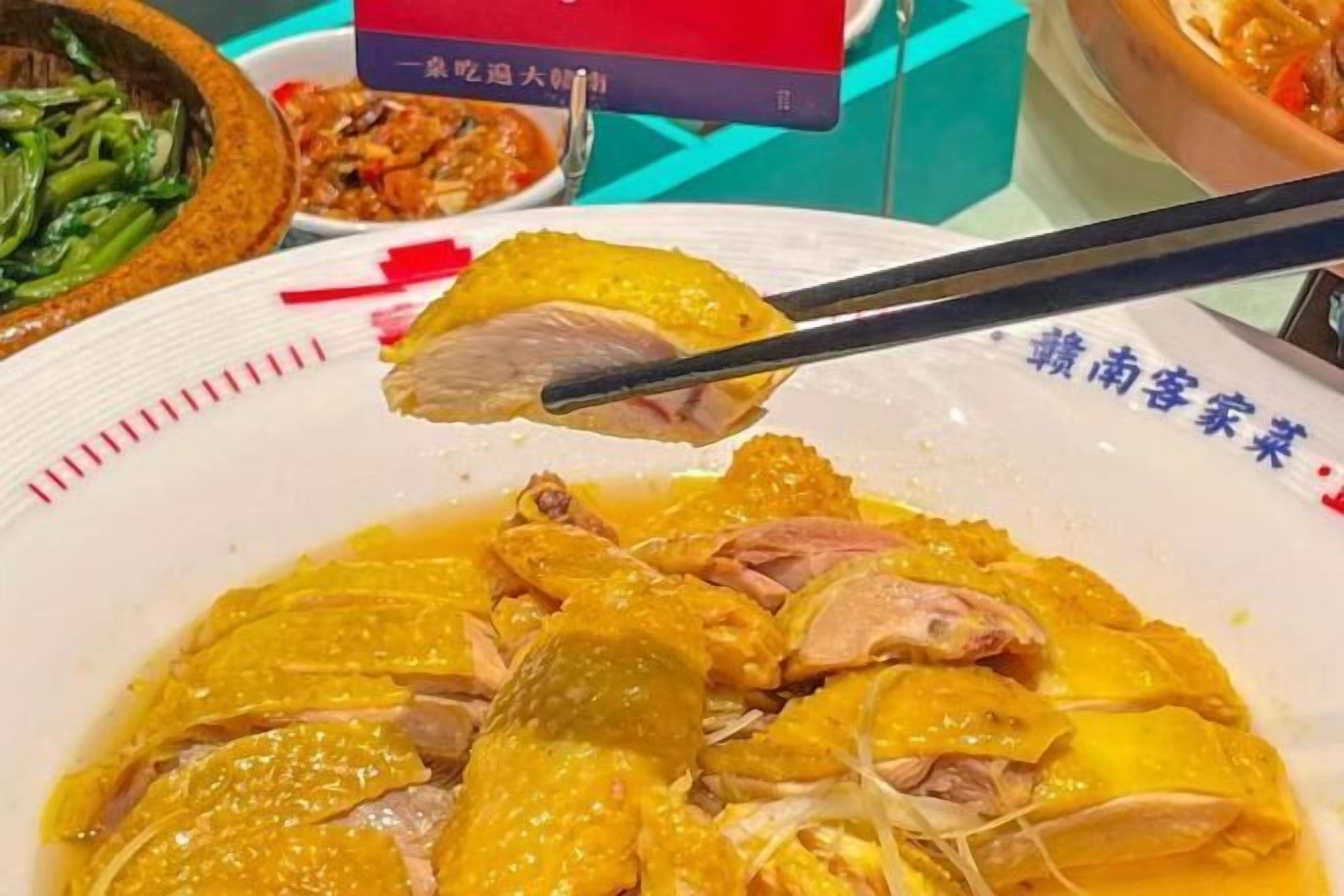 A bowl of chicken with a yellow sauce, accompanied by a red box and a bowl of vegetables.