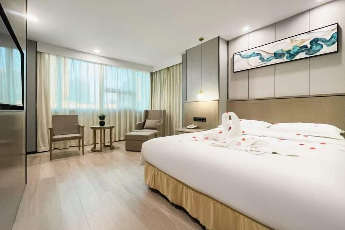 A modern hotel room with a large bed, a desk, a chair, and a window with curtains.