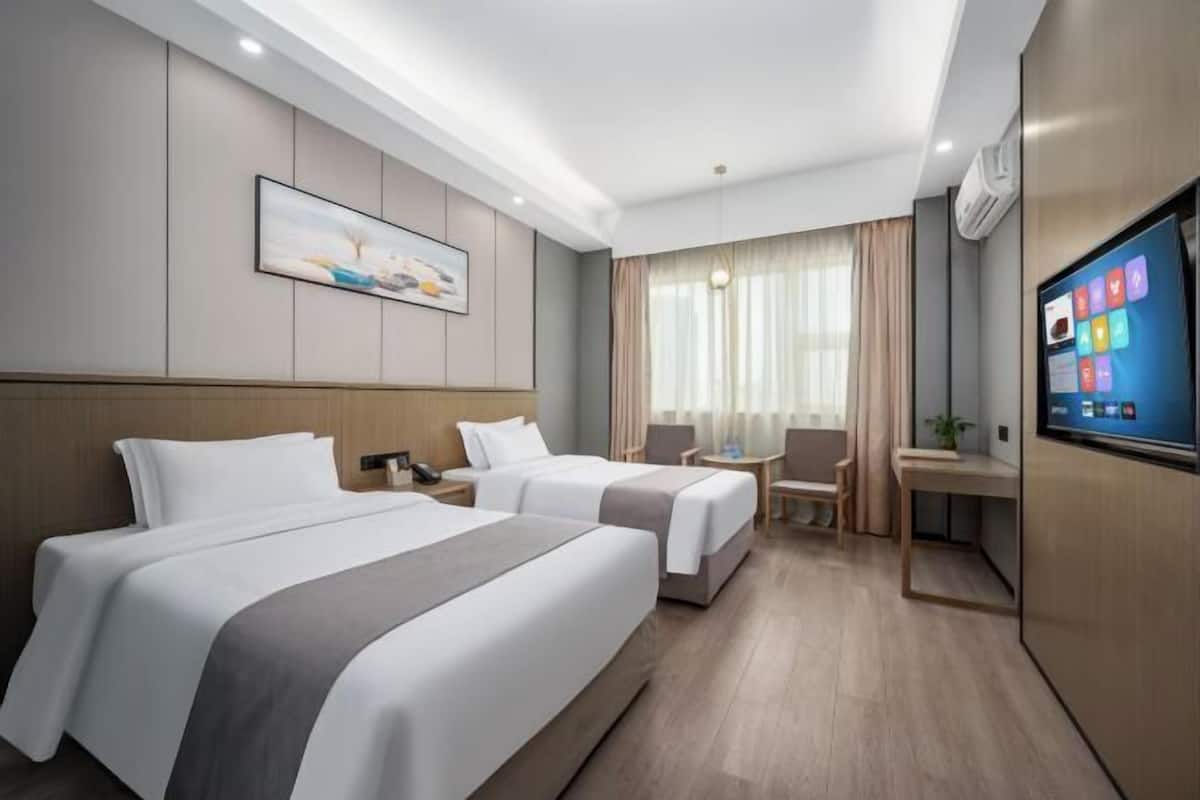 A hotel room with two beds, a desk, a chair, a TV, and a painting on the wall.