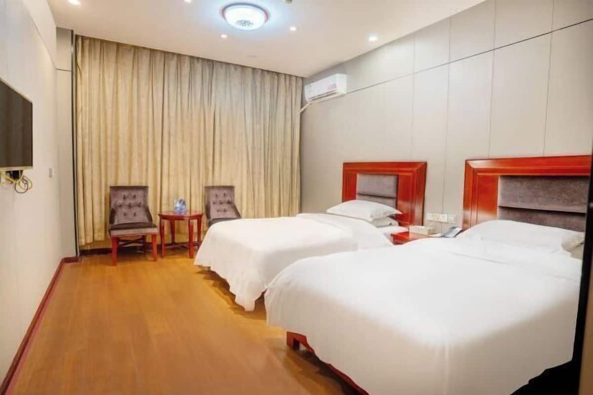 A hotel room with two beds, a small table, a chair, and a television.