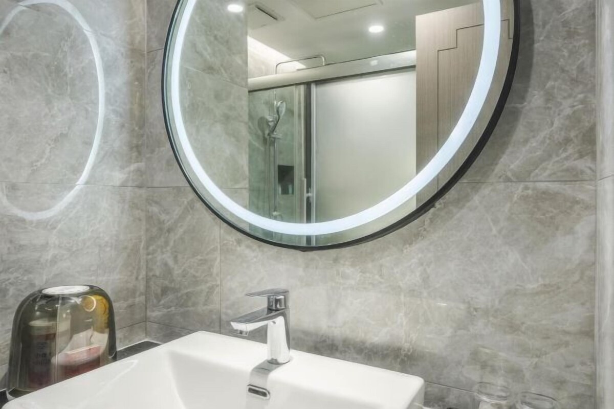 Une salle de bain avec un miroir rond, un lavabo blanc et une cabine de douche en verre.