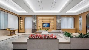 Een moderne hotellobby met een centrale zithoek, een receptiebalie en een groot televisiescherm.