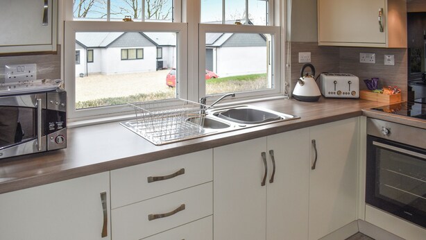 Una cocina moderna con armarios blancos, electrodomésticos de acero inoxidable y una ventana con vistas al exterior.