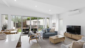 A modern living room with a sofa, TV, and dining area. - Stillwater on Stockton, 57B Stockton St - complete luxury in the heart of town (Nelson Bay)