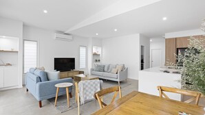 A modern living room with a sofa, TV, and coffee table. There is a kitchen area with a fridge and cabinets. - Stillwater on Stockton, 57B Stockton St - complete luxury in the heart of town (Nelson Bay)