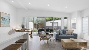 A modern living room with a grey sofa, wooden coffee table, and a dining area with a white table and chairs. - Stillwater on Stockton, 57B Stockton St - complete luxury in the heart of town (Nelson Bay)