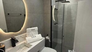Un baño moderno con tocador de mármol, cabina de ducha con mampara de vidrio y un espejo grande con iluminación integrada.