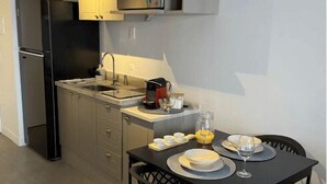 Cocina compacta con refrigerador, microondas y lavamanos. Hay una mesa de comedor con platos y un vaso.