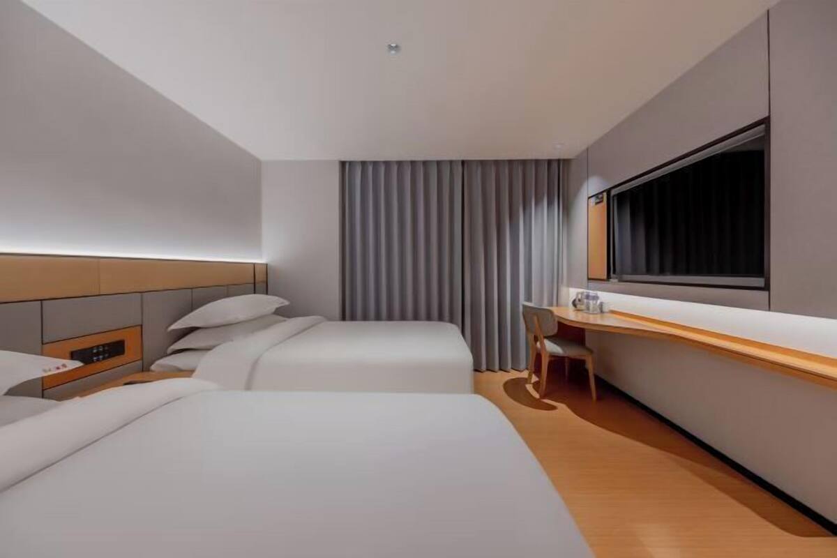 A hotel room with two beds, a desk, a chair, a large window, and a curtain.
