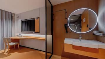 A hotel room with a desk, chair, and a round mirror with lights.
