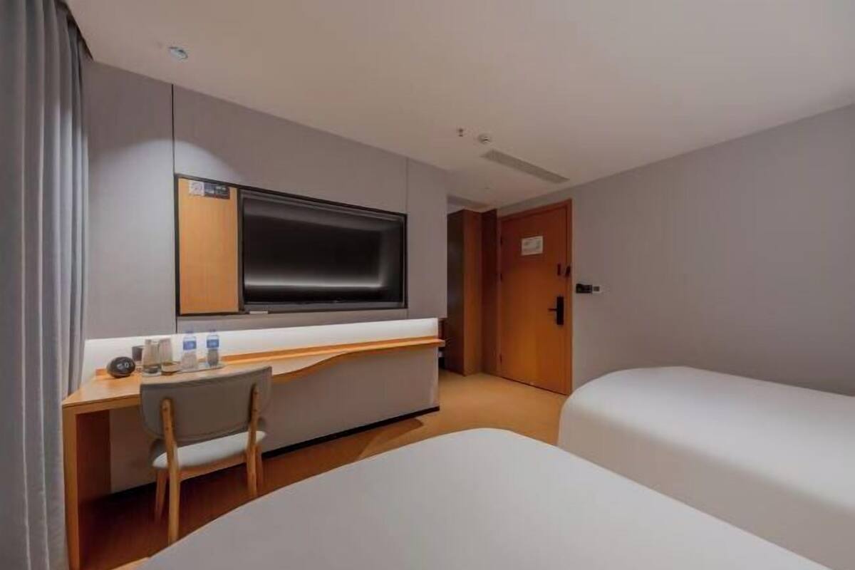 A hotel room with a bed, a desk with a chair, a television, and a door.