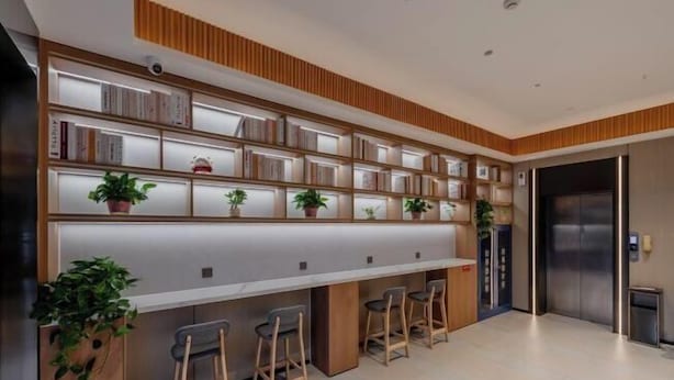 A modern kitchen with a long counter, bar stools, and a built-in bookshelf with plants. - 8 Days Hotel (Minhang Jiaotong University Branch) (Shanghai)