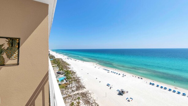 A beach view from a balcony with a clear sky, a sandy beach, and a pool area. - Sterling Reef 905 (Panama City Beach)