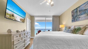 Ein Hotelzimmer mit einem grossen Bett, einem Deckenventilator, einem an der Wand befestigten Fernseher und einem Balkon mit Meerblick.