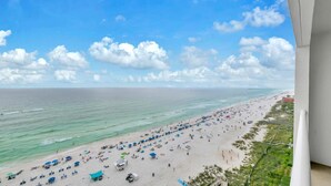 Ein Strand mit Sonnenschirmen und Menschen, ein klarer Himmel und ein Pier in der Ferne.