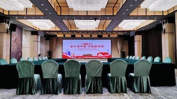 A conference room with a large screen, rows of chairs, and a stage.