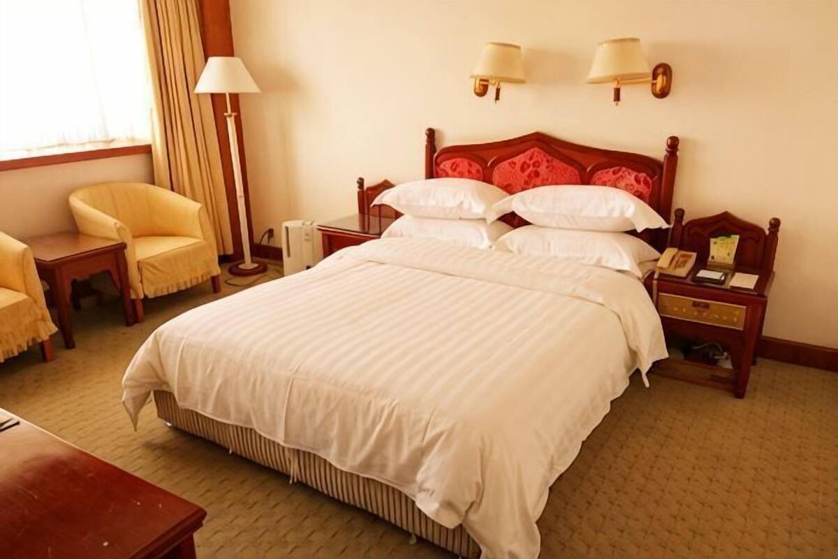 A hotel room with a large bed, bedside tables, a chair, and a lamp.