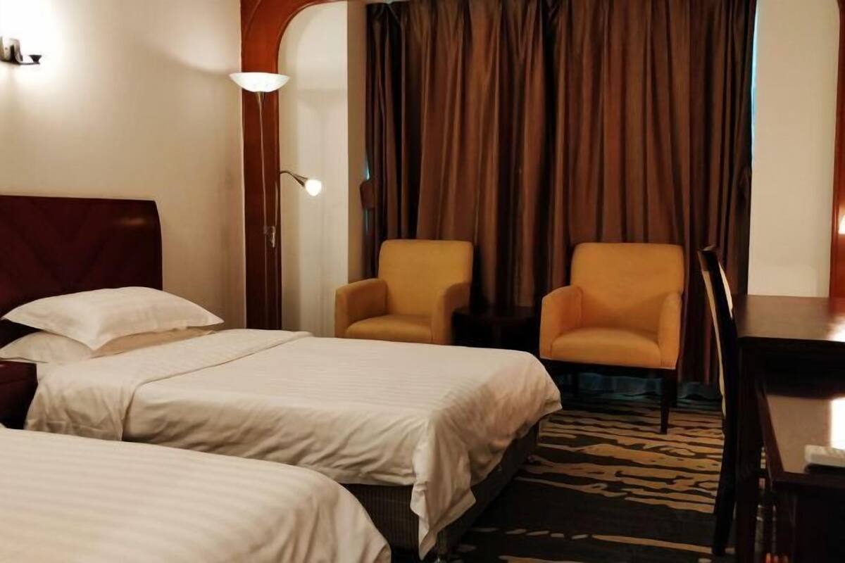 A hotel room with two beds, a desk, a chair, and a large window with curtains.