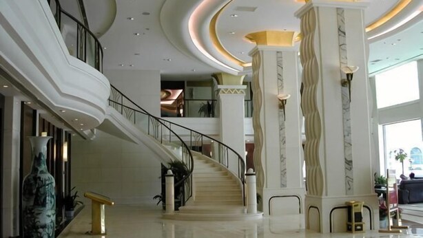Un'ampia hall con una scalinata a forma di ferro di cavallo, colonne in marmo e un soffitto alto con illuminazione a scomparsa.