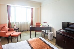 A hotel room with a bed, a desk, a chair, a television, and a heater. - Jinshan Hotel (Shanghai)