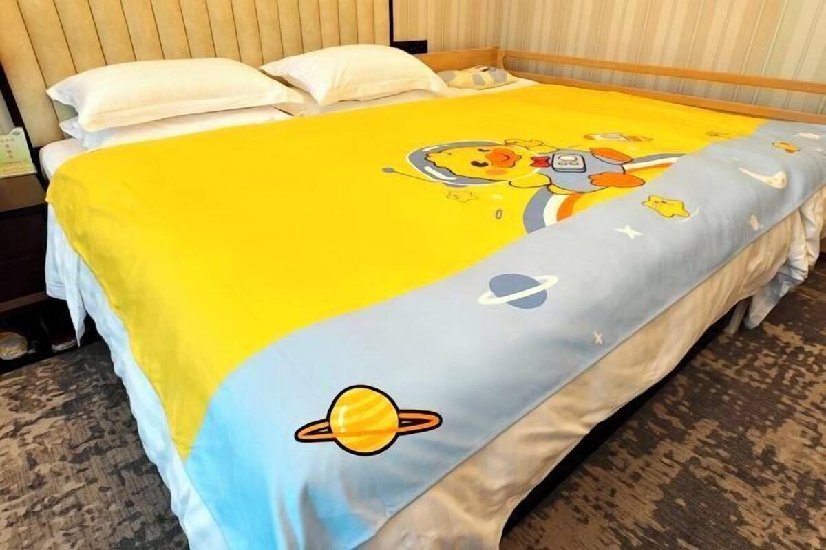 A bed with a yellow and blue bedspread featuring cartoon characters and planets.