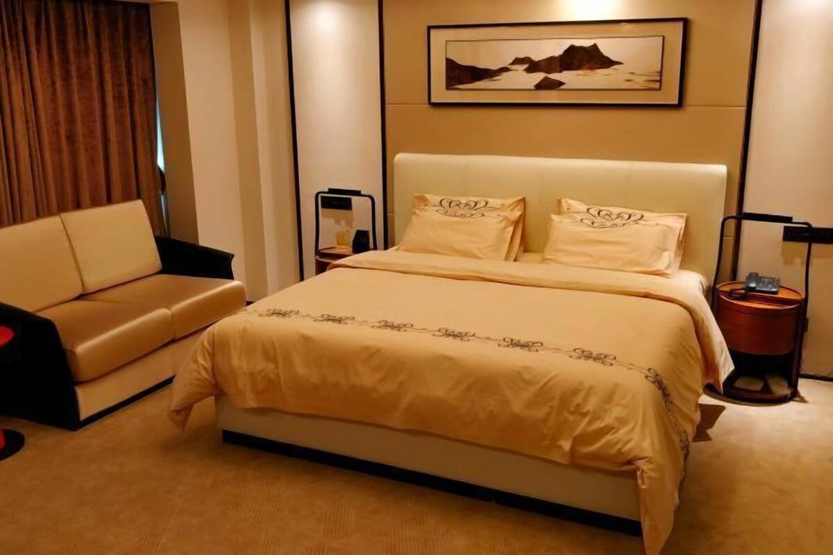 A hotel room with a bed, a sofa, a bedside table, a lamp, and a framed picture on the wall.