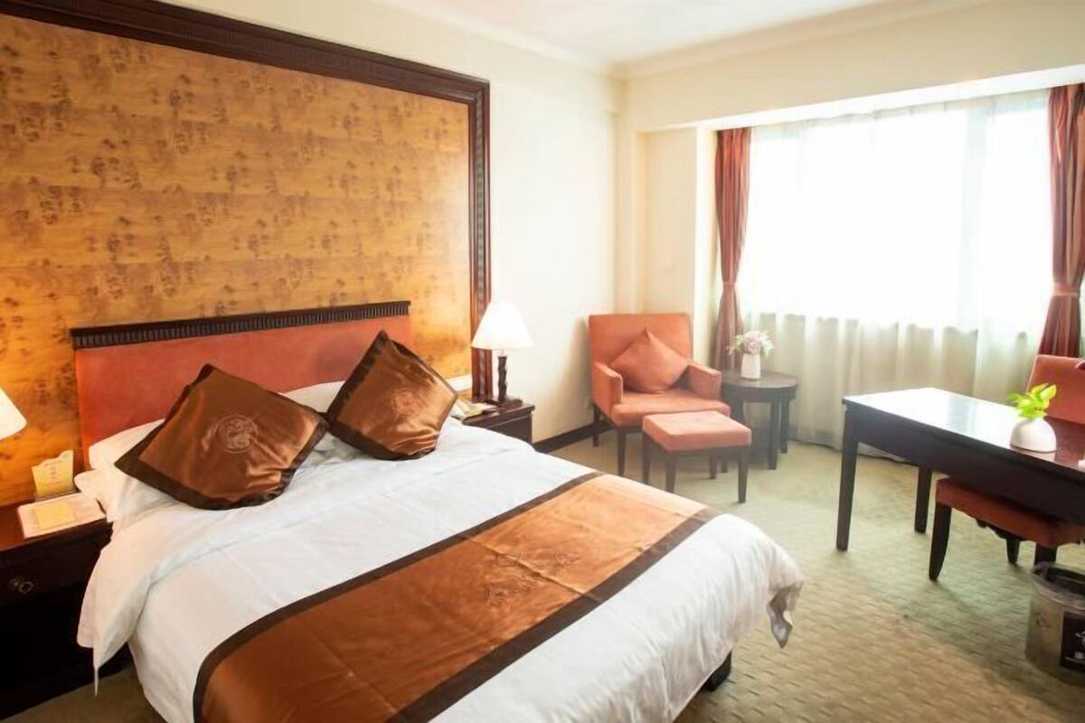 A hotel room with a large bed, a desk, a chair, and a view of the outdoors.