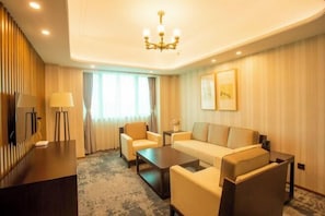 A hotel room with a sofa, armchairs, a coffee table, a TV, and a chandelier. - Jinshan Hotel (Shanghai)