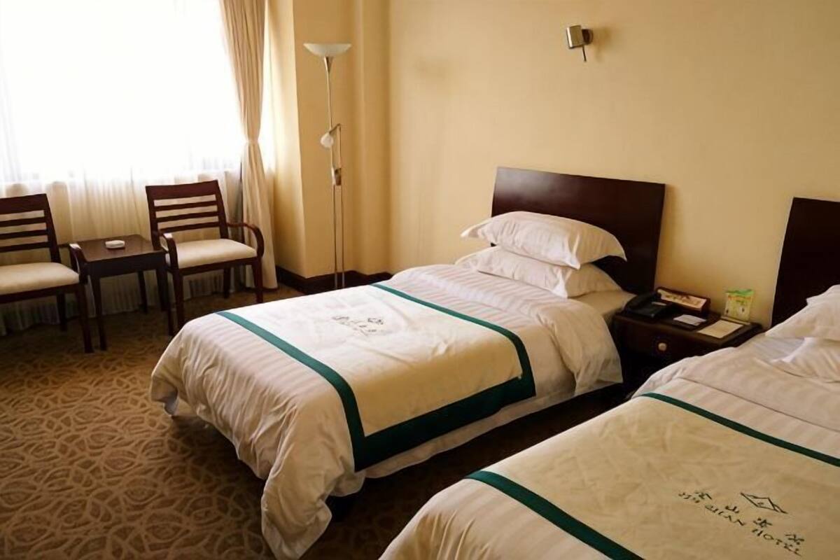 A hotel room with two beds, a desk, chairs, a lamp, and a nightstand.