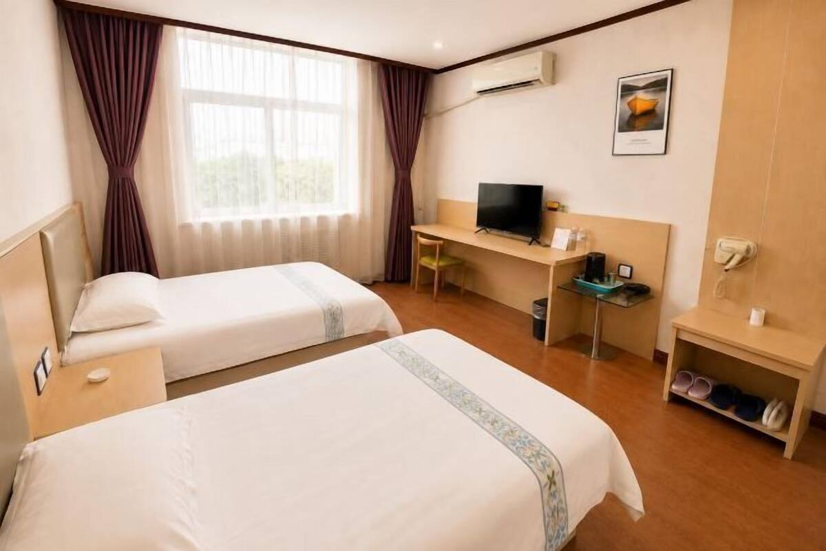 Een hotelkamer met twee bedden, een bureau met een computer, een televisie en een schoenenrek.