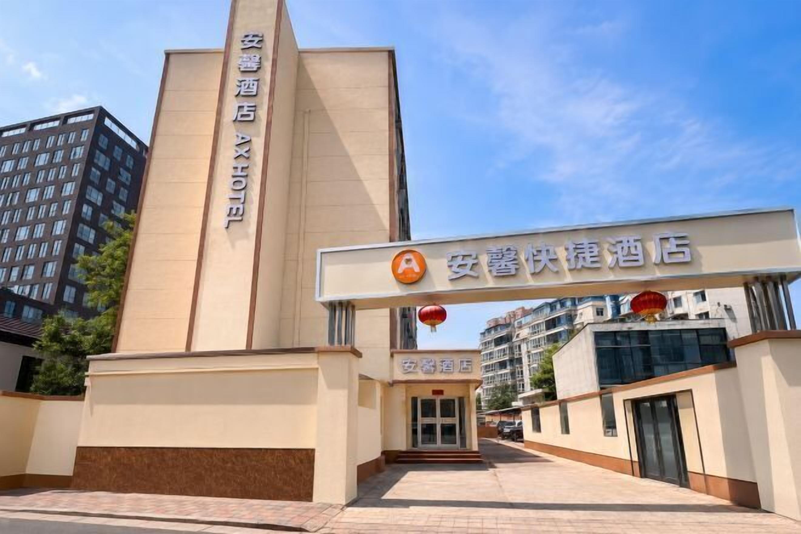 A hotel entrance with a vertical sign, a horizontal sign above the entrance, and a building in the background.