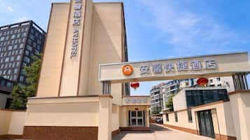 A hotel entrance with a vertical sign, a horizontal sign above the entrance, and a building in the background.
