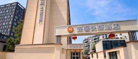 A hotel entrance with a vertical sign, a horizontal sign above the entrance, and a building in the background.