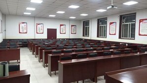 Un aula con filas de escritorios y sillas, paredes blancas y carteles educativos.